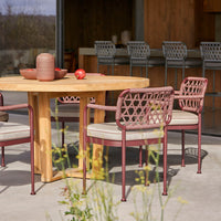 "Round wooden table with warm brown tones, surrounded by patterned burgundy and cream chairs in an outdoor setting."