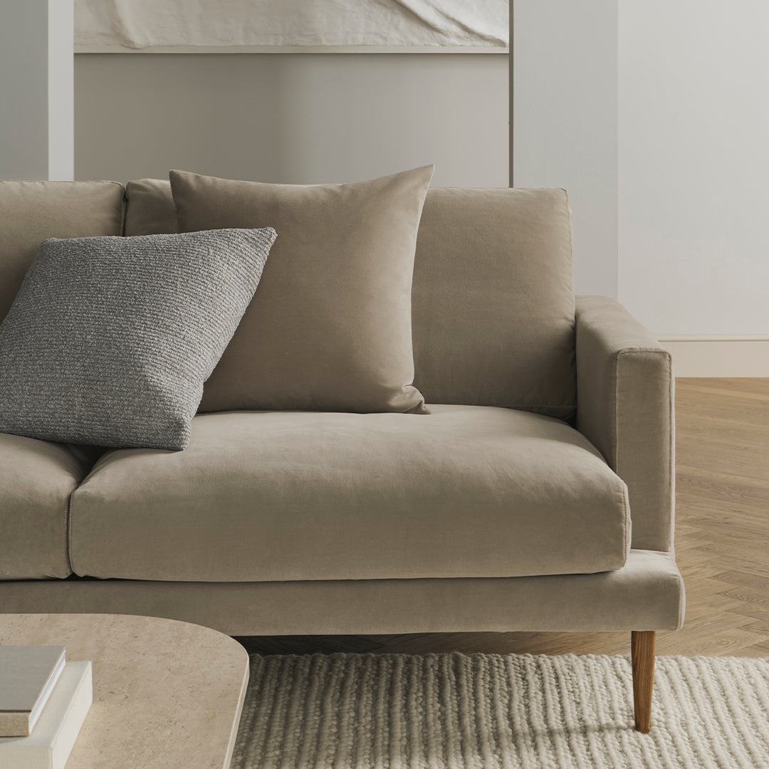 Beige sofa with a soft texture and gray accent pillow, set against a neutral, minimalist background.