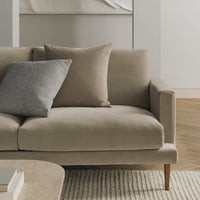 Beige sofa with a soft texture and gray accent pillow, set against a neutral, minimalist background.