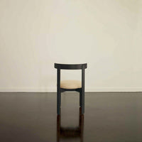 Black wooden chair with a beige cushion, set against a neutral background and dark polished floor.