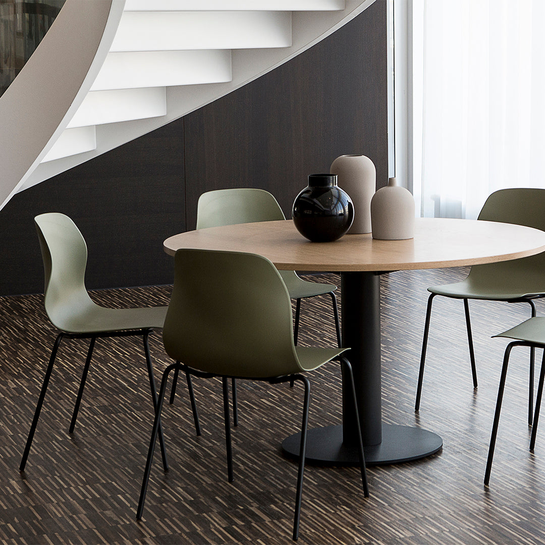 Green chairs around a round wooden table, set against dark wood flooring and light-colored decorative vases.
