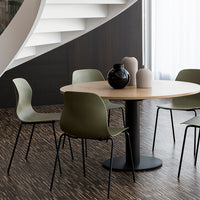 Green chairs around a round wooden table, set against dark wood flooring and light-colored decorative vases.