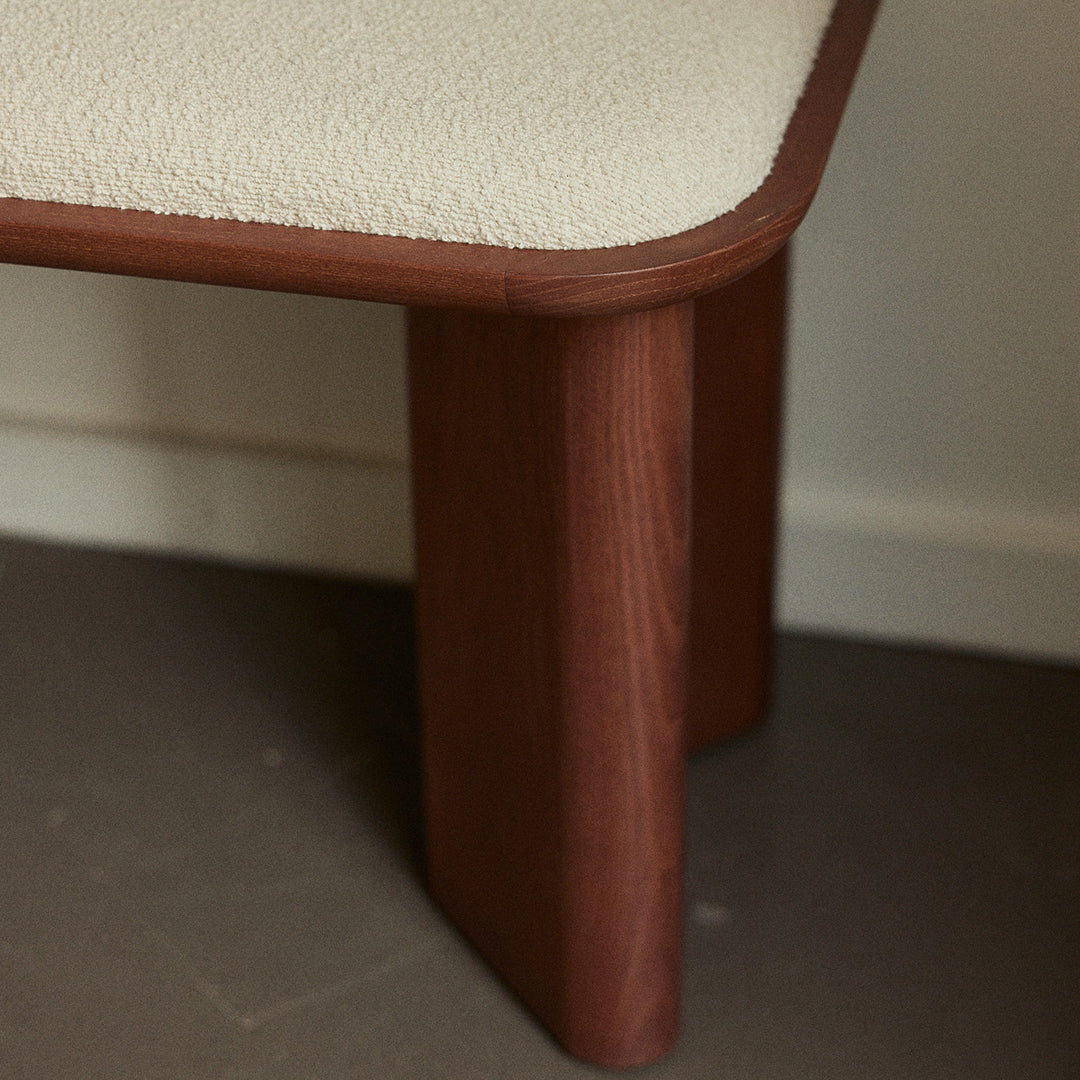 Cream upholstery with a smooth curved edge, paired with rich brown wooden legs, showcasing a minimalist design.