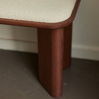 Cream upholstery with a smooth curved edge, paired with rich brown wooden legs, showcasing a minimalist design.