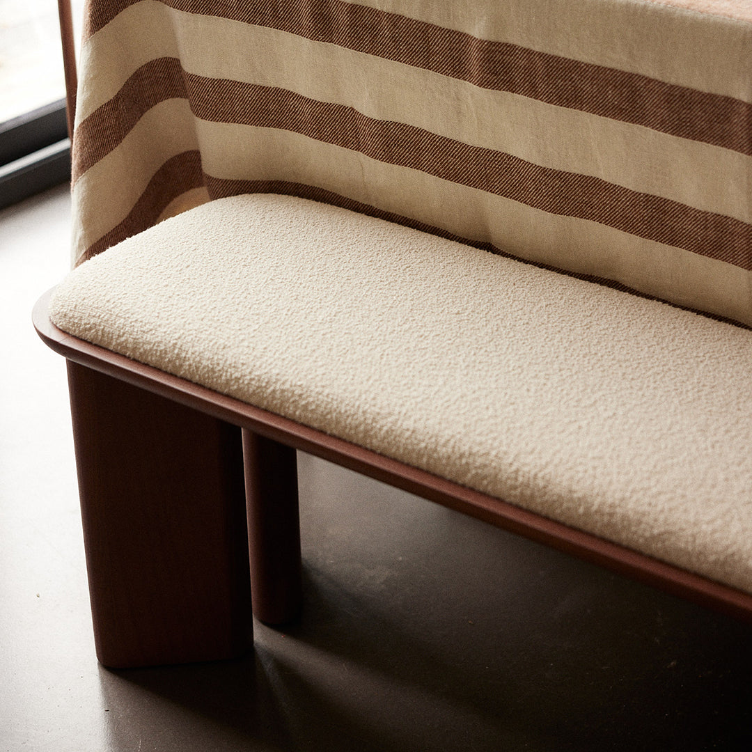 Neutral beige cushion on a wooden bench, complemented by a striped brown and cream fabric backdrop.