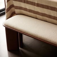 Neutral beige cushion on a wooden bench, complemented by a striped brown and cream fabric backdrop.