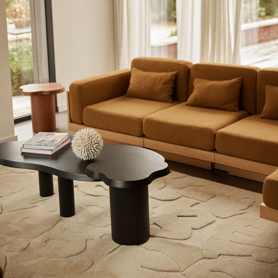 Stylish brown couch with beige cushions, black sculptural coffee table, and textured cream rug in a modern living room.