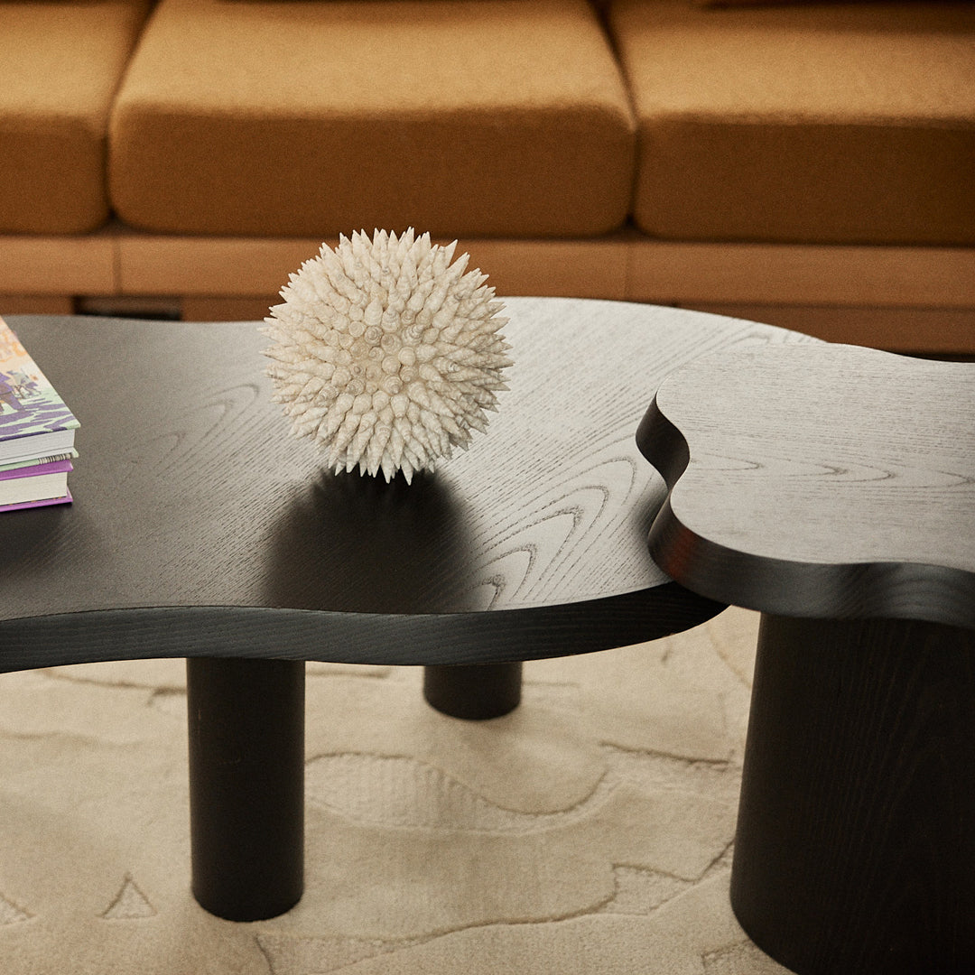 Black abstract coffee table with unique curves and rounded legs, sitting on a textured beige rug. 