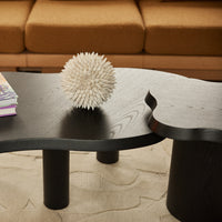 Black abstract coffee table with unique curves and rounded legs, sitting on a textured beige rug. 