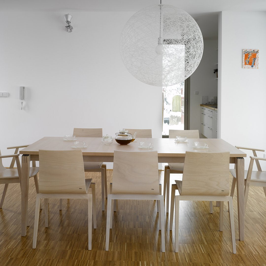 Light wood dining table with minimalist design, complemented by beige chairs and bright white walls. Modern and airy ambiance.
