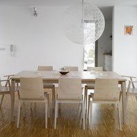 Light wood dining table with minimalist design, complemented by beige chairs and bright white walls. Modern and airy ambiance.