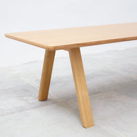 Light natural wood table with smooth, minimalistic design and angled legs on a neutral background.