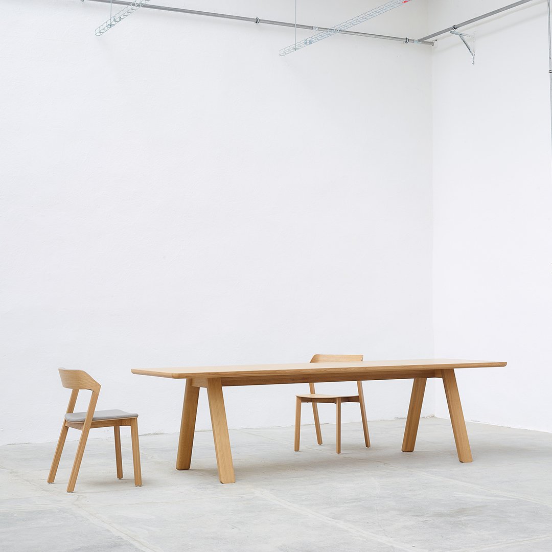 Minimalist wooden dining table and chairs in light wood finish against a clean, white backdrop.