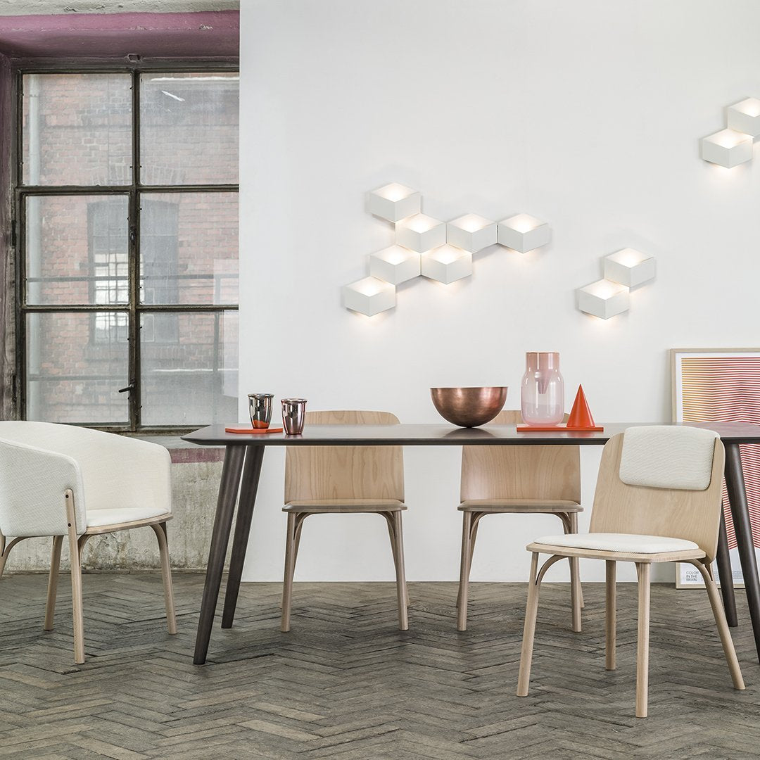 Modern dining set featuring light wood and white chairs, a black table, and colorful decor accents in pink and orange.