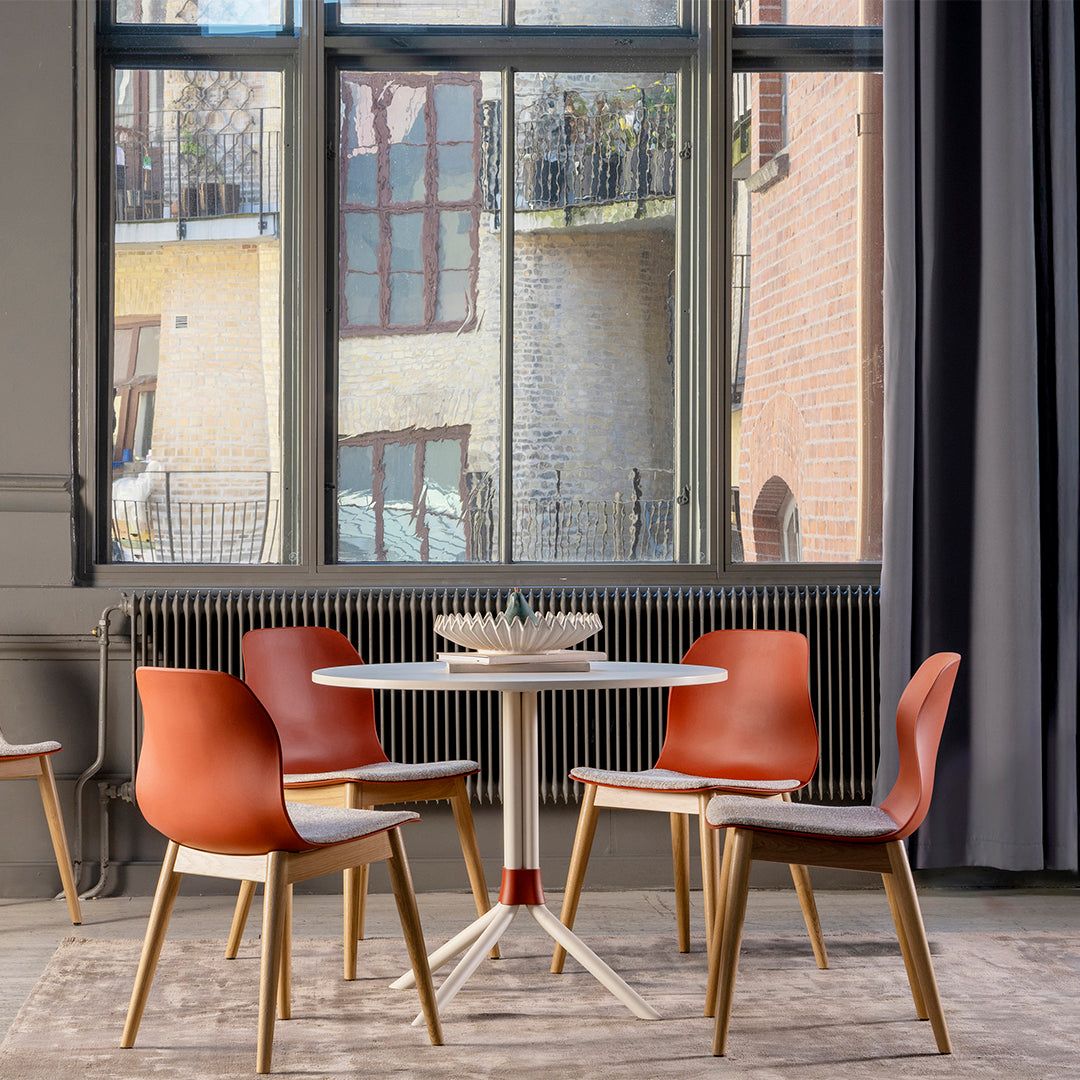 "Modern dining set featuring orange chairs, light wood legs, and a white circular table on a neutral rug."