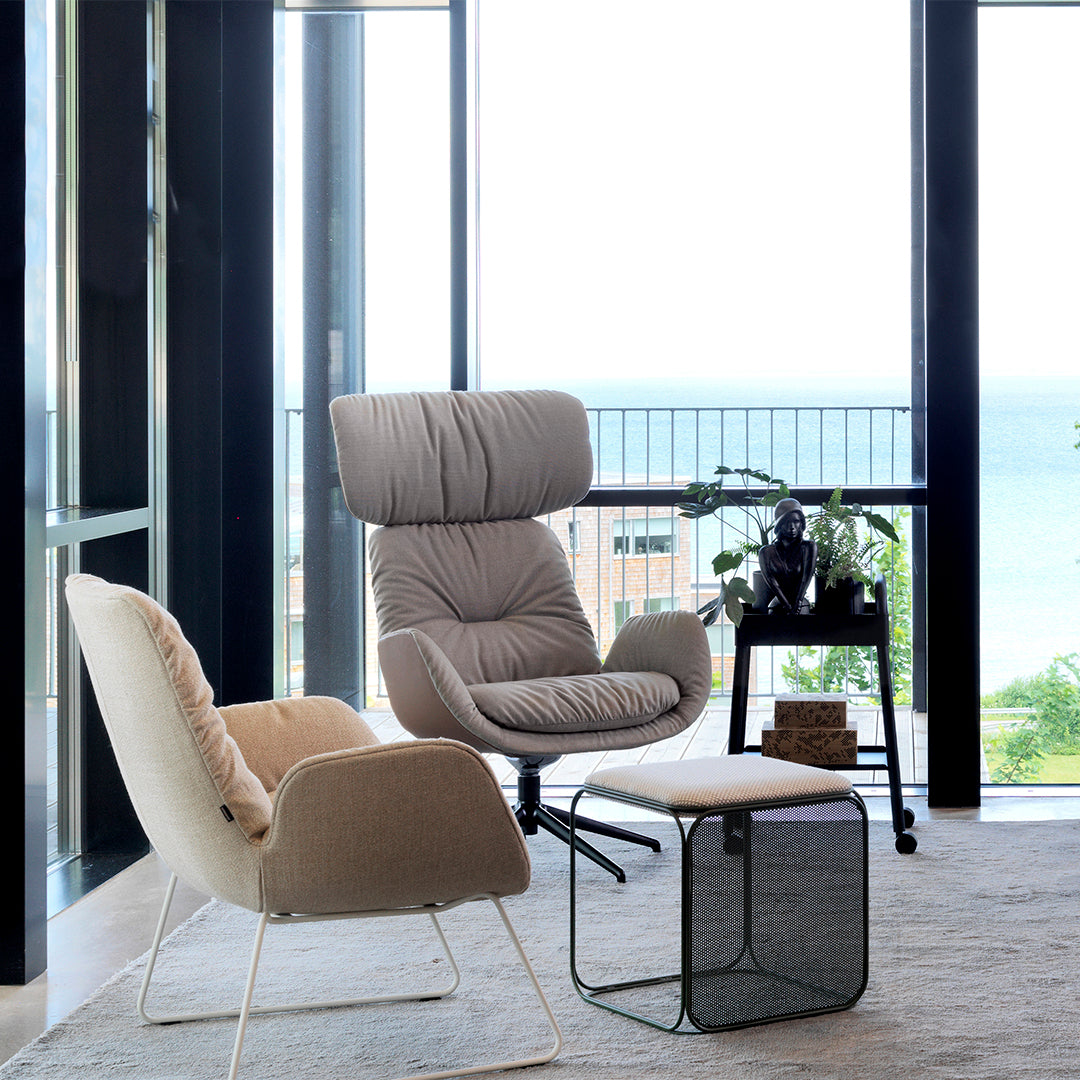 Heavily textured beige and light brown armchairs with a dark metal side table in a modern, airy setting.