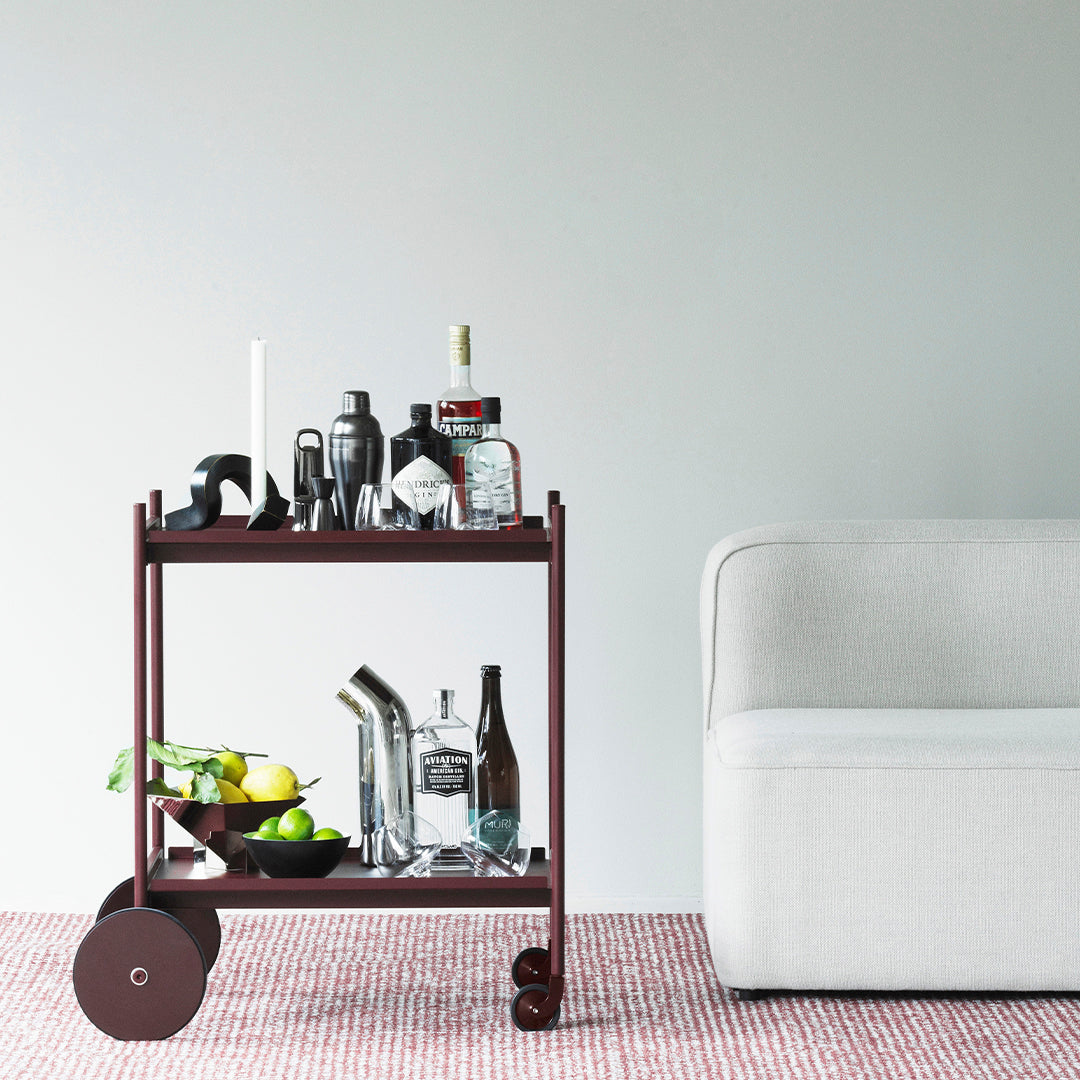 Brown bar cart with black accents, featuring a gray couch on a patterned red and white rug.