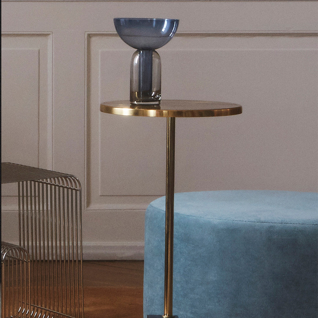Blue glass bowl atop a sleek gold-accented side table, beside a soft blue ottoman, all against a neutral backdrop.