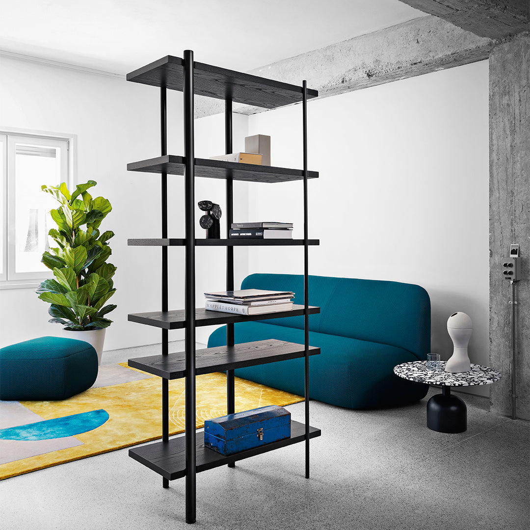 Modern black shelving unit with dark wood shelves, accented by teal couch and vibrant yellow and blue area rug.