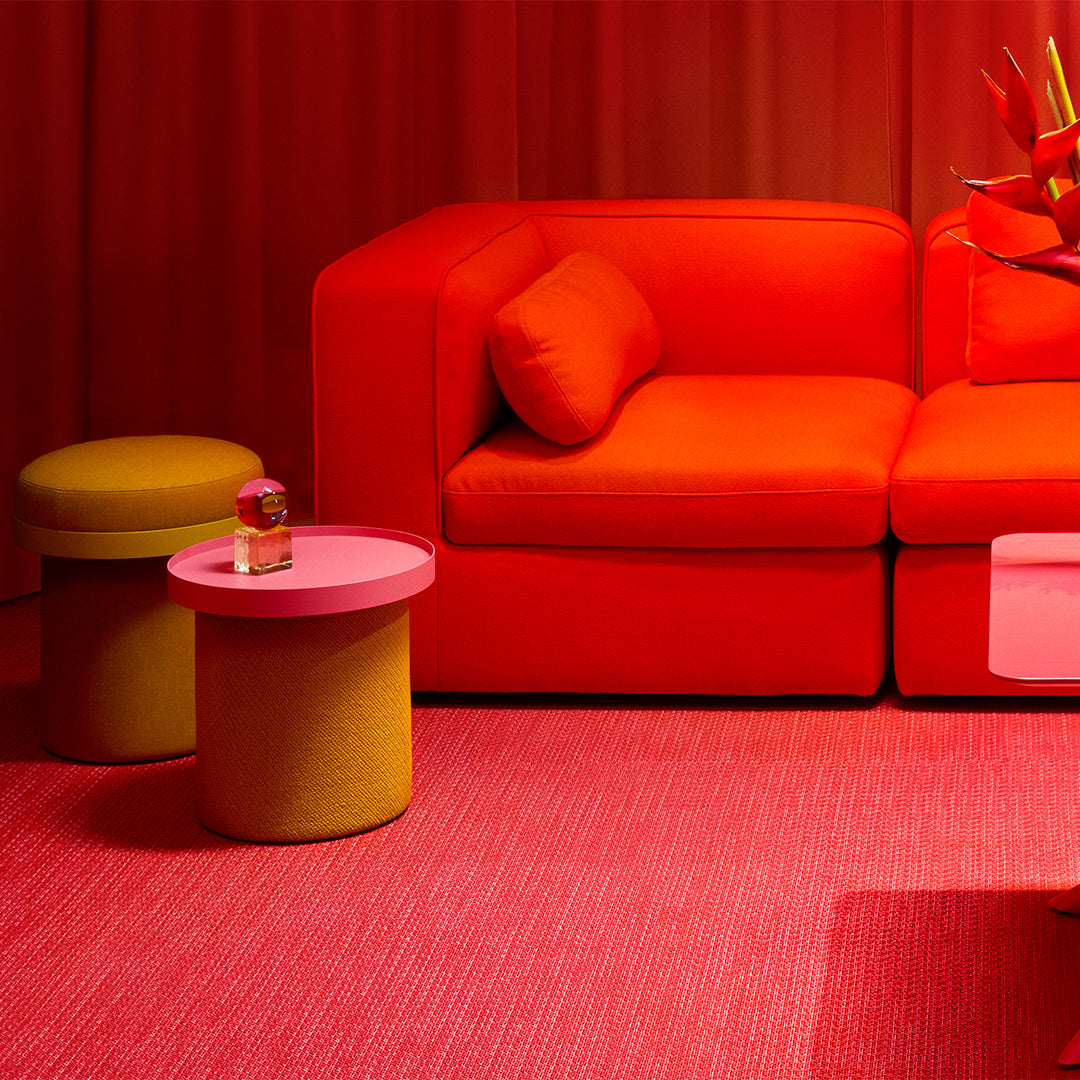 Vibrant red sofa with orange cushions, yellow and pink accent tables, and a textured pink rug, creating a bold color palette.