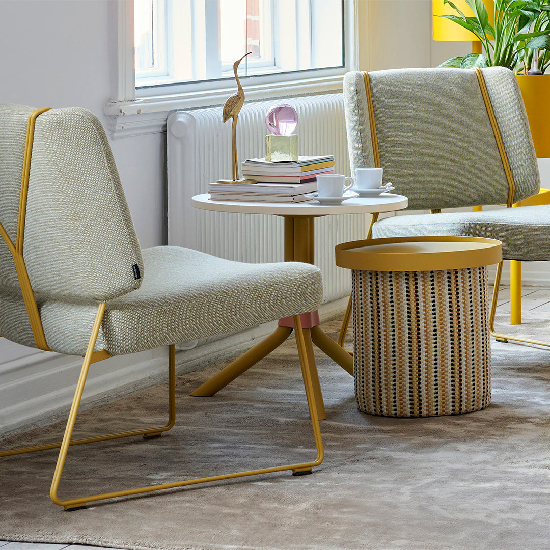 Light grey upholstered chairs with yellow accents, round white table, and a striped woven side table in neutral tones.