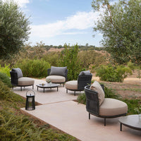 Modern patio seating in soft beige cushions with black frames, surrounded by lush greenery and a serene outdoor setting.