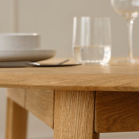 Light oak table with a smooth finish, complemented by neutral-toned plates and clear glassware. Rustic yet modern appeal.