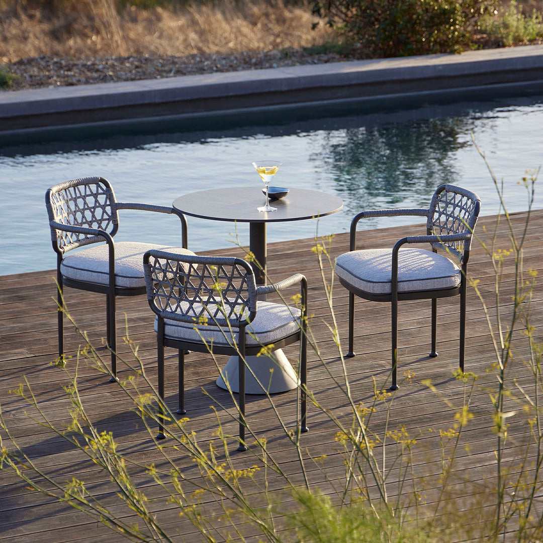 Four modern outdoor chairs with a geometric pattern, gray cushions, and black metal frames, set beside a pool.