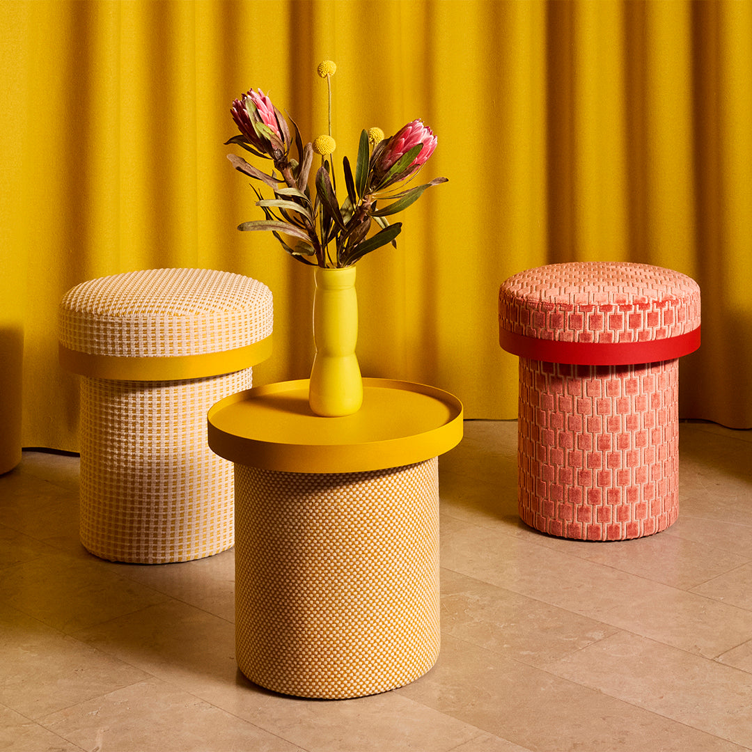 Colorful stools in yellow, white, and pink with geometric patterns against a vibrant yellow backdrop.