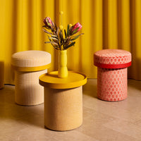 Colorful stools in yellow, white, and pink with geometric patterns against a vibrant yellow backdrop.