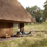 Rustic brown thatched roof with natural wood tones and dark gray outdoor furniture, set in a green grassy landscape.