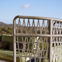 Grey woven patio furniture with a diamond pattern against a backdrop of green cushions and blue sky.