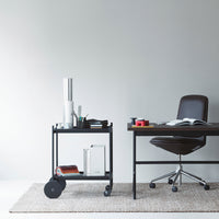 Modern black metal cart with a clean design, featuring a wooden desk and neutral tones in a minimalist workspace.