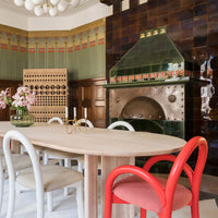 Modern dining area featuring earthy tones, green accents, and a bright red chair against patterned wooden walls.