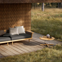 "Modern outdoor sofa in black with neutral cushions and a round wooden table, set against a textured brown wall."