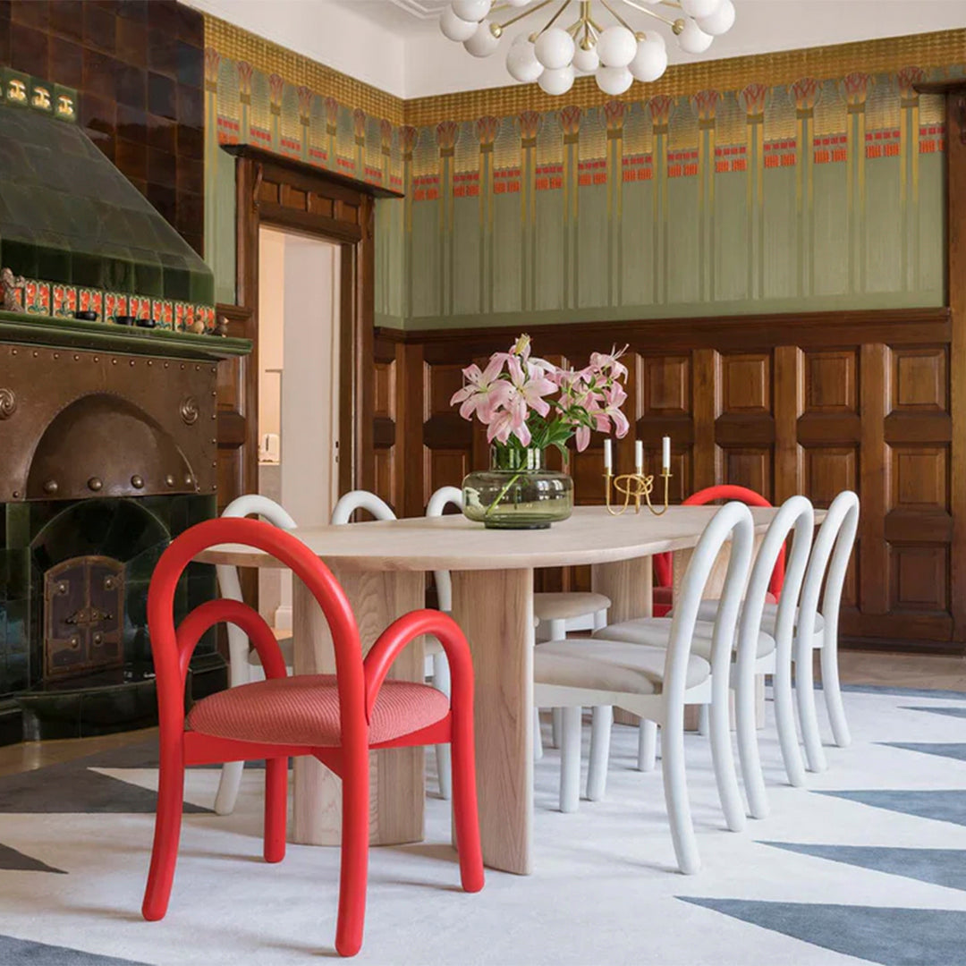 Elegant red and white chairs on a patterned gray and white rug in a stylish dining room with green and wooden accents.