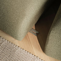 Textured olive green upholstery with a subtle pattern, paired with a light beige woven rug on a wooden floor.