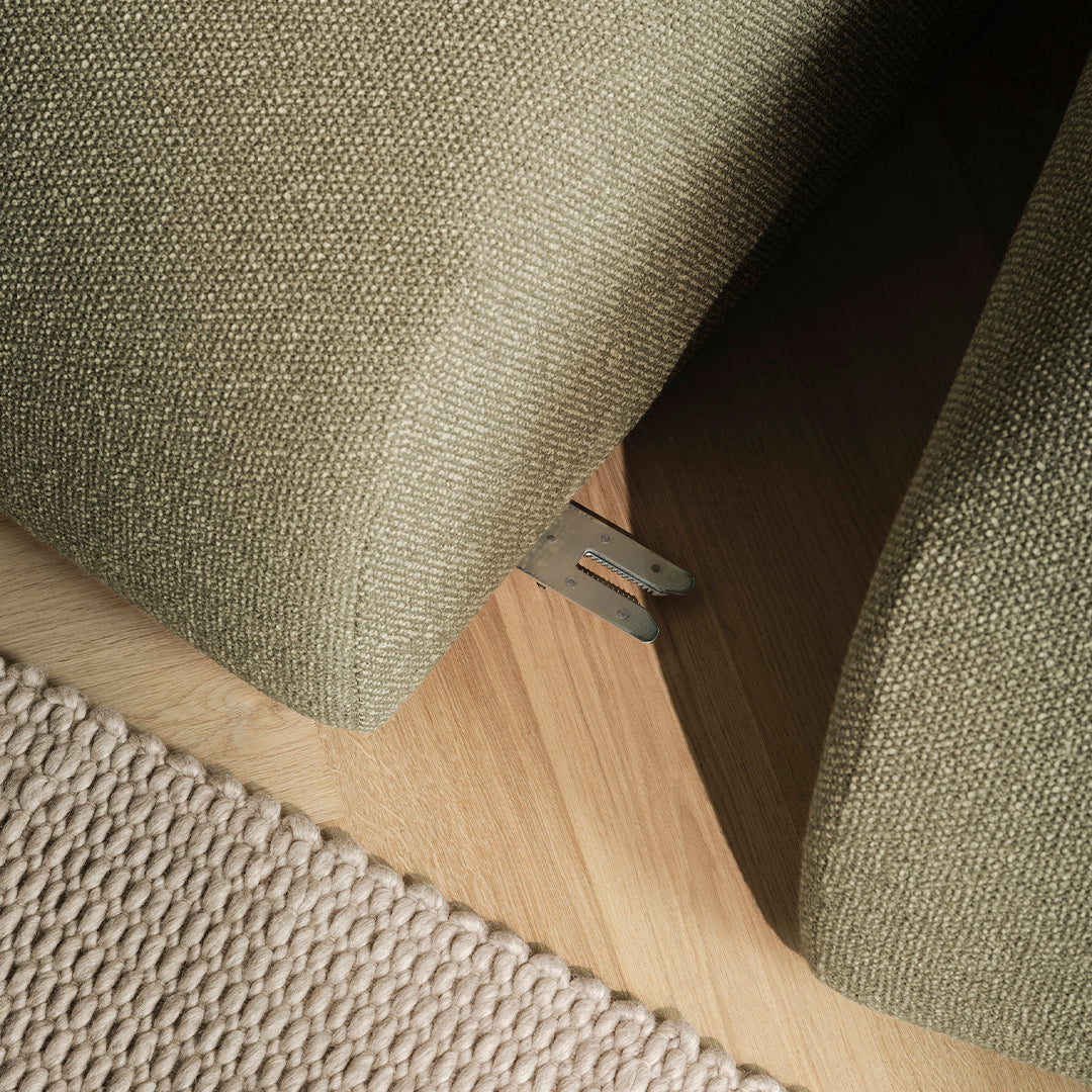 Green textured upholstery paired with a beige, woven rug on a light wood floor, showcasing subtle elegance.