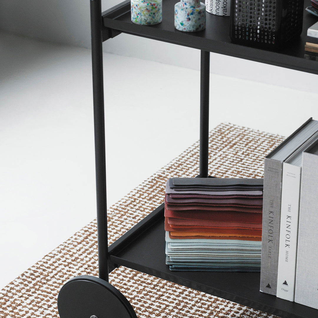 Stylish black cart with colorful stacked fabrics in gradient shades and a patterned rug in soft neutral tones.