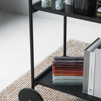 Stylish black cart with colorful stacked fabrics in gradient shades and a patterned rug in soft neutral tones.