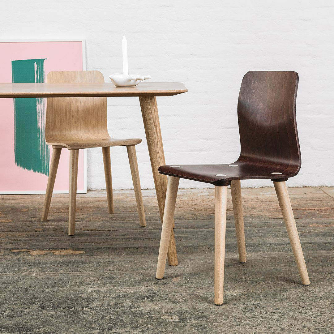 Wooden chairs in dark and light finishes, set against a pink and green patterned backdrop. Modern design elements.