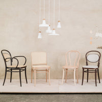 Four stylish chairs in black, light wood, and natural cane against a neutral background with pendant lighting.