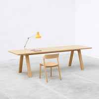 Light wood table and chair set with a bright yellow lamp, minimalist design against a white wall and concrete floor.