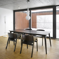 Modern black dining table with sleek wooden legs, surrounded by minimalist black chairs and a bright white pendant light.
