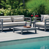 Gray outdoor sofa set with beige cushions featuring subtle stripes, accented by vibrant red flowers and a sleek coffee table.