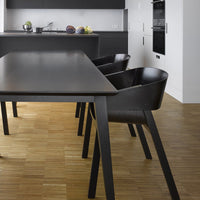 Modern black dining table with matching black chairs, set against a warm, light wood floor in a sleek kitchen.