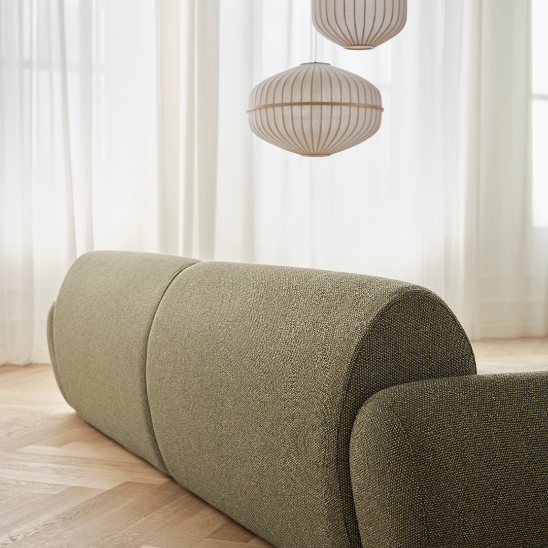 Green textured sofa with rounded edges, complemented by soft, natural light filtering through sheer white curtains.