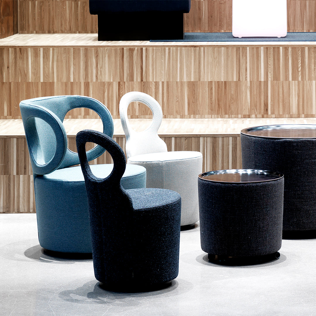Modern chairs in soft blue, white, and dark grey fabrics with unique circular armrests and smooth textures.