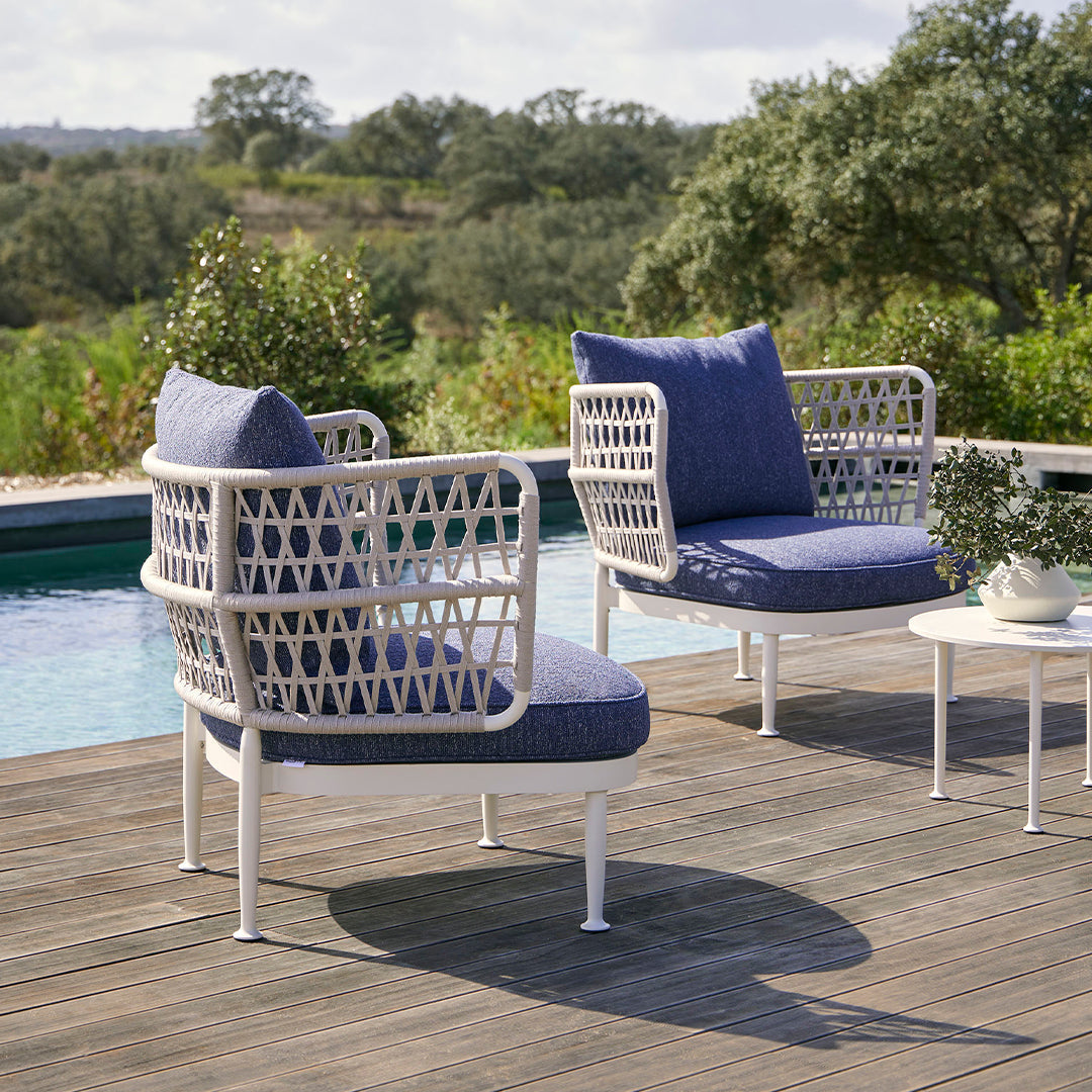"White wicker patio chairs with navy cushions and a modern geometric pattern, set against a scenic outdoor backdrop."
