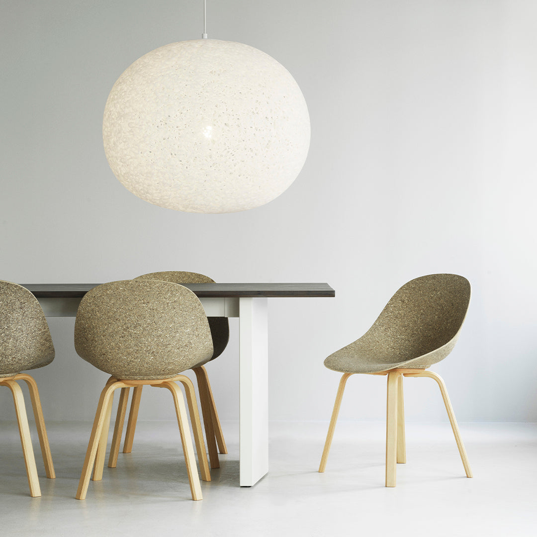 Light gray and beige dining chairs with wood legs, paired with a round white pendant light over a minimalistic table.